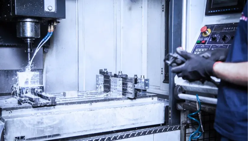 Precyzyjne wiercenie w metalu na maszynie CNC. Chłodziwo rozpryskuje się podczas obróbki. Operator w rękawicach steruje procesem.