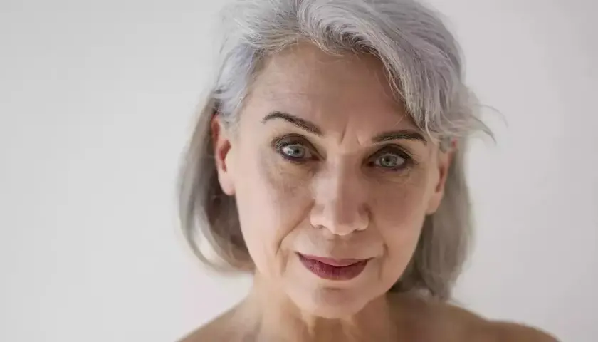 Primo piano di una donna con capelli grigi e pelle matura, che mostra i segni del tempo con grazia.