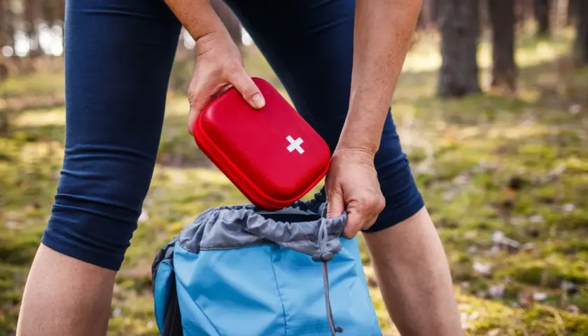 Person packt roten Erste Hilfe Set Inhalt in blauen Rucksack für Wanderung.