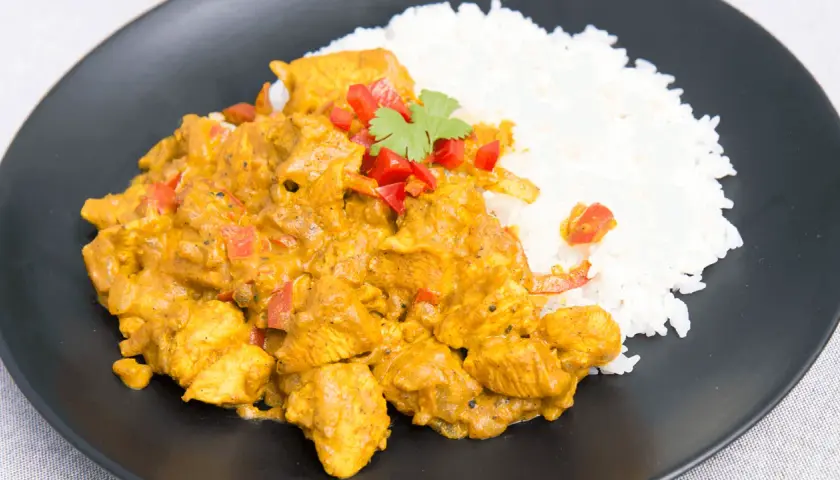 Aromatyczny kurczak curry z ryżem, doprawiony papryką i świeżą kolendrą, podany na czarnym talerzu.