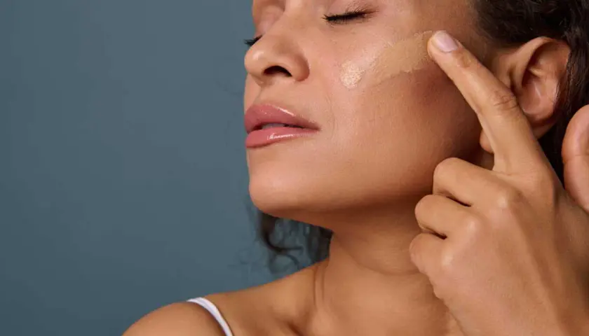 Application d'un fond de teint pour un maquillage teint parfait. Une femme applique délicatement le produit sur sa joue.