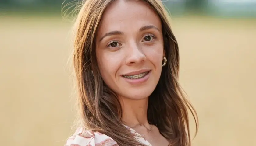 Wiktoria z Rolnik szuka żony, uśmiechnięta, z aparatem na zębach, w kwiecistej sukience, na tle pola.