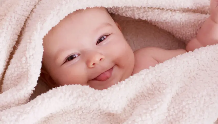Uśmiechnięta Aurelia wtulona w miękki kocyk, wystawia języczek.