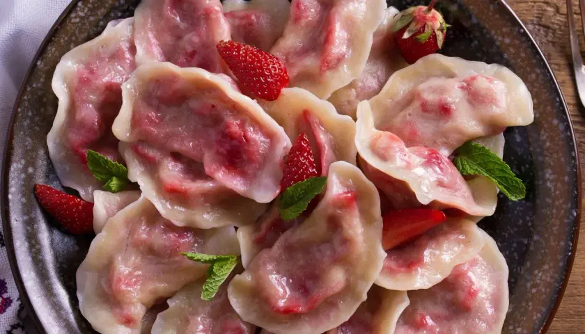 Pyszne pierogi z truskawkami, ozdobione świeżymi owocami i miętą, prezentują się apetycznie na talerzu.