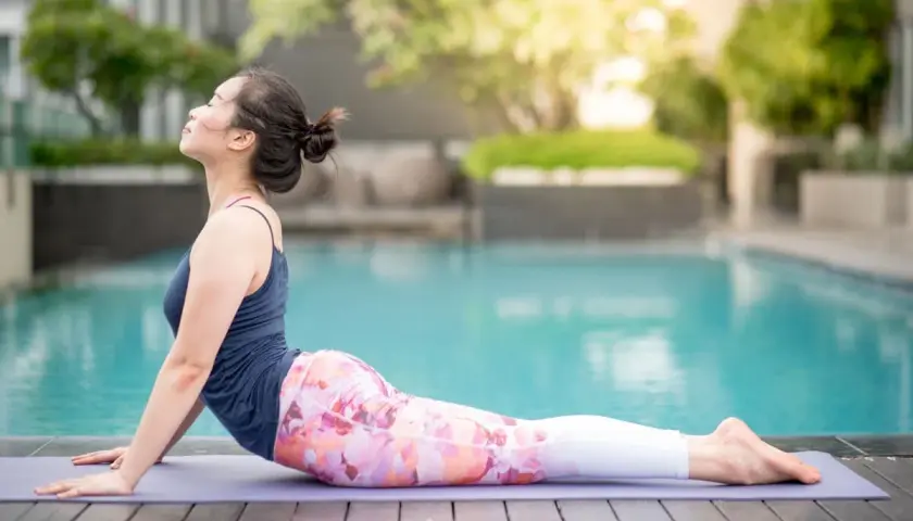 Kobieta w pozycji bhujangasana na macie przy basenie, zrelaksowana, z głową uniesioną do góry.