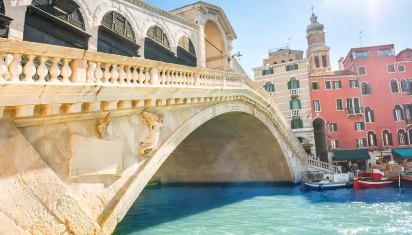 Le célèbre pont du Rialto à Venise, avec ses arches majestueuses et ses bâtiments colorés en arrière-plan, se reflète dans les eaux turquoise du Grand Canal.