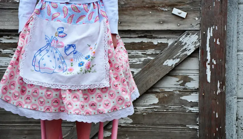 A vintage apron skirt pattern with a girl watering flowers, set against a rustic wooden background.