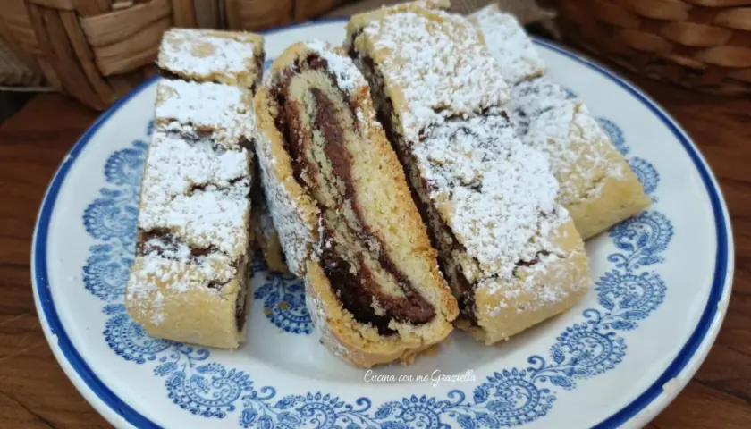 Fette di biscotti della nonna con ripieno di crema al cioccolato, spolverati di zucchero a velo, su un piatto decorato.