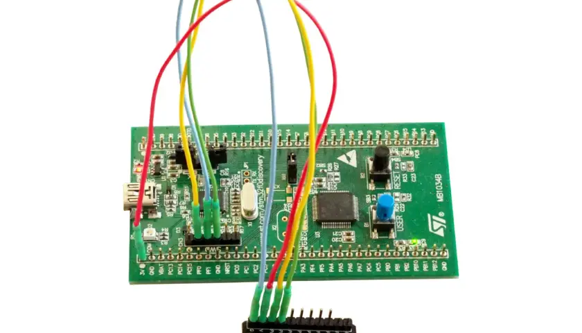 Zielona płytka STM32 z kolorowymi przewodami podłączonymi do małego modułu.