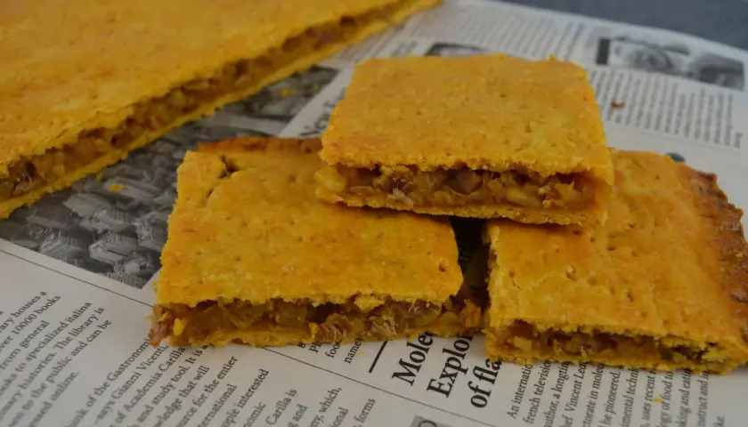 Coca amb tonyina, un delicioso pastel salado relleno de atún y cebolla, servido sobre un periódico.