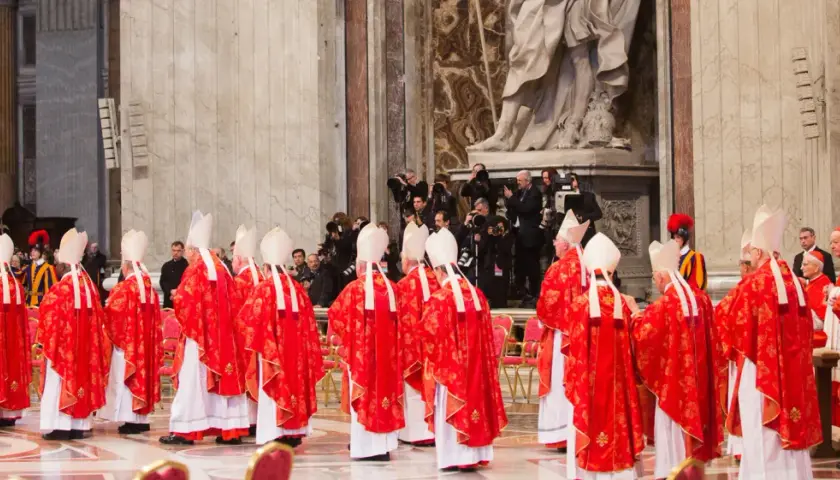 Kardinäle in roten Gewändern und Mitra stehen in einer Kirche. Dies ist ein Moment, der an ein Konklave erinnert, wo ein neuer Papst gewählt wird.