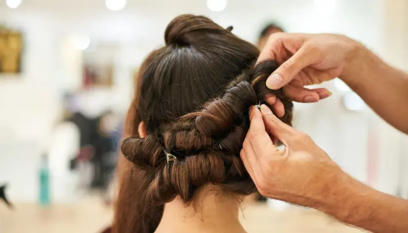 Hårstylist hjälper till att rulla håret på spolar för att skapa volym och lockar.