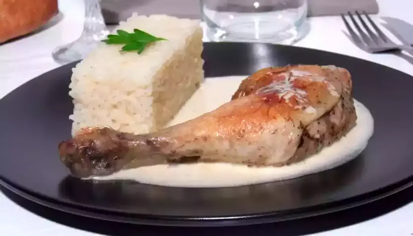 Un délicieux poulet à la crème, servi avec une portion de riz blanc et une feuille de persil. Un plat savoureux et réconfortant.