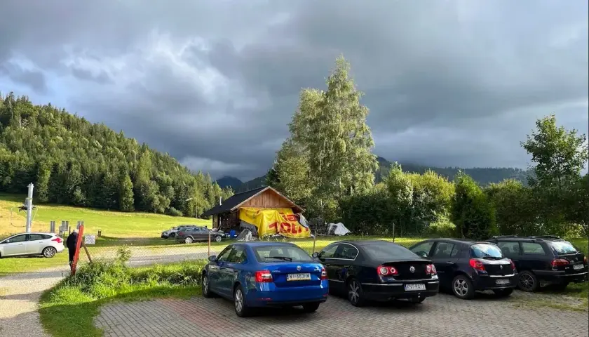 Samochody na parkingu pod Babią Górą, w tle las i chmury.