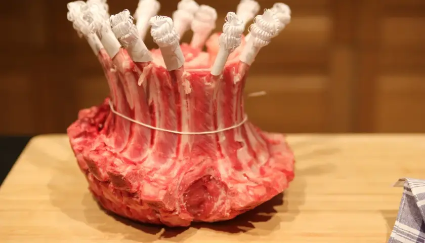 Une couronne d'agneau crue, prête pour la cuisson, avec les os protégés par du papier blanc.