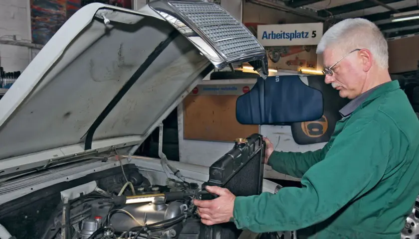 Mechanik w zielonym kombinezonie wykonuje wymianę chłodnicy krok po kroku w warsztacie.