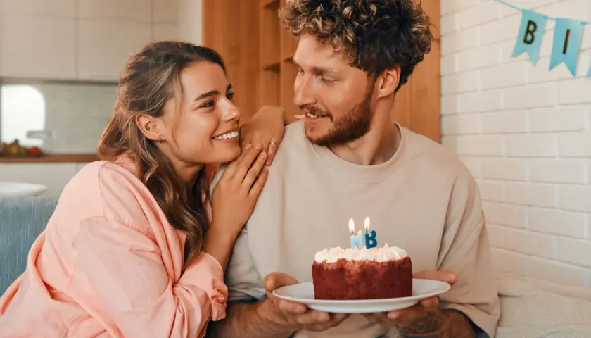 Pareja sonriente celebra un cumpleaños con un pastel. Ideas de frases bonitas para felicitar cumpleaños a tu pareja.