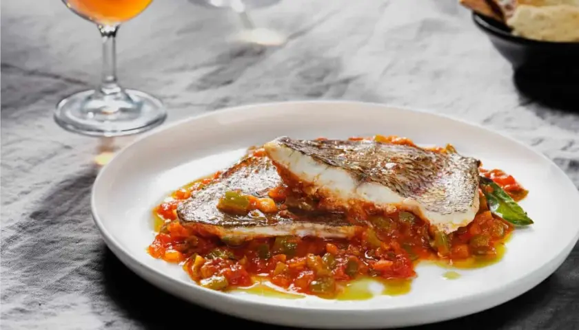 Deliciosa urta a la roteña servida en plato blanco, con vino y pan tostado al fondo.