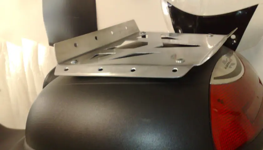 Piatto metallico forato, parte di un portapacchi moto fai da te, fissato su un bauletto nero.