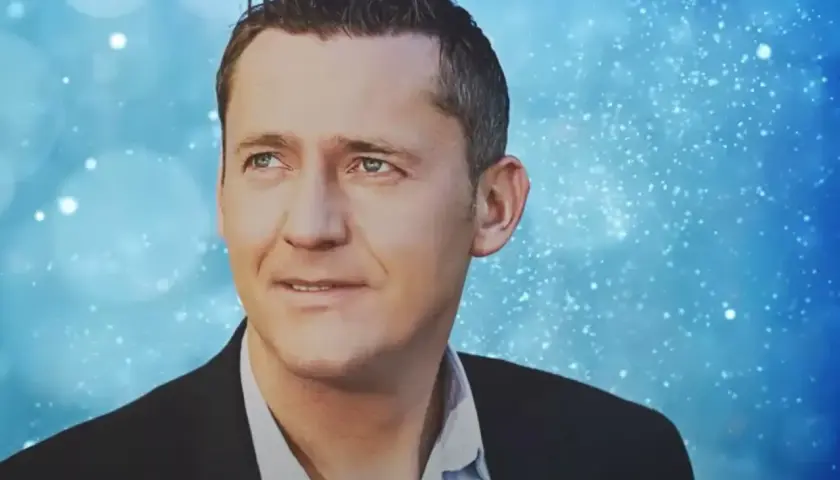 Portret Adama Chroli w garniturze na tle niebieskich, migoczących świateł.