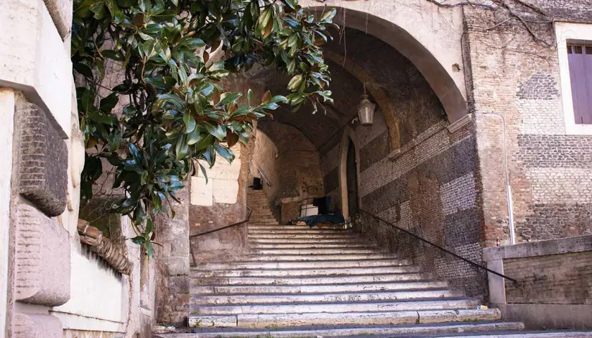 Scalinata romana con alberi di magnolia e un arco antico. Un'idea per cosa vedere a Roma domani, un angolo suggestivo e storico.