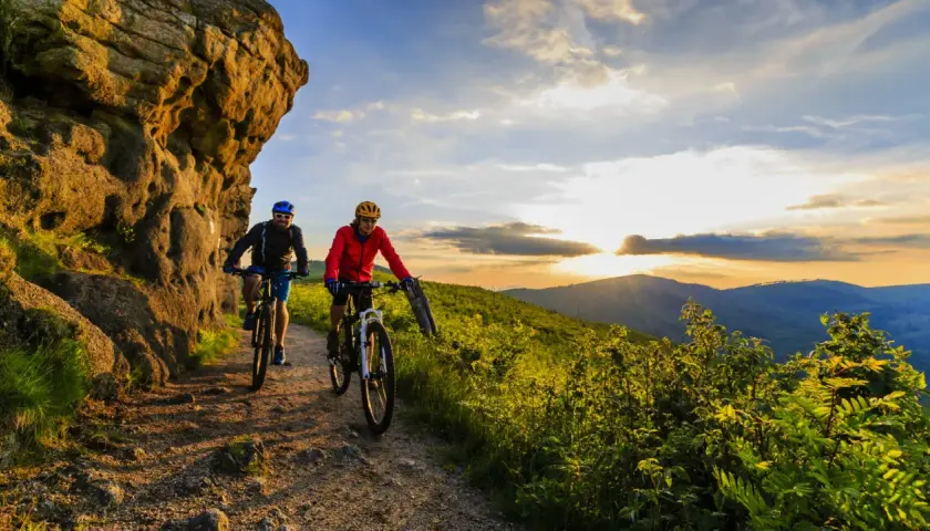 Dwóch rowerzystów przemierza górski szlak o zachodzie słońca, odkrywając piękno krajoznawstwa.