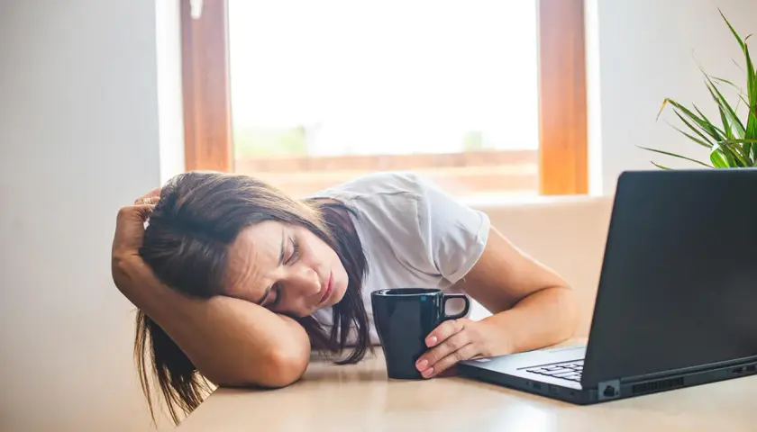 Donna esausta con tazza e laptop, forse cerca rimedi della nonna per la carenza di ferro.