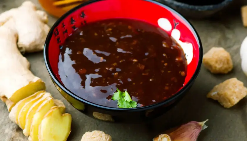 Sos teriyaki przepis: miseczka z ciemnym sosem, obok imbir, czosnek, cukier i miód. Idealny do dań azjatyckich.