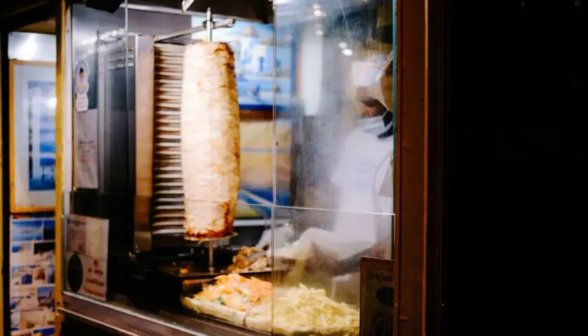 Obracający się pionowo kebab z frytkami i sałatką w witrynie.