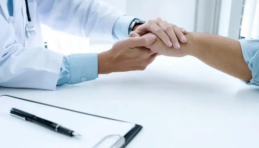 Lekarz trzyma pacjenta za rękę, okazując wsparcie. Dymista cena usług medycznych nie powinna być barierą w otrzymaniu pomocy.