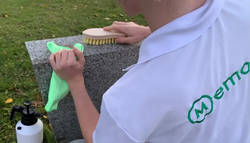Person cleaning a granite gravestone with a green cloth and a brush.