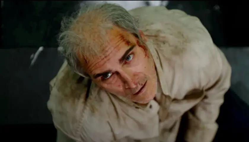 Un uomo con i capelli grigi e ferite sul viso, vestito di una camicia sporca, guarda in alto con espressione spaventata. Beau ha paura, spiegazione visiva.