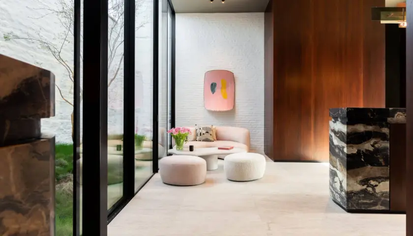 Un elegante soggiorno con pavimenti in marmo moderni, divano rosa, pouf e un tavolino bianco.