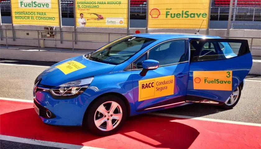Coche azul en circuito con pegatinas Shell FuelSave, promocionando conducción eficiente.