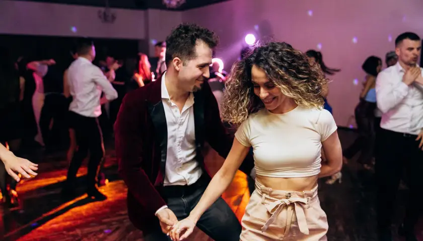 Para tańczy w rytm muzyki, ciesząc się wspólnym tańcem użytkowym. W tle widać innych bawiących się ludzi.