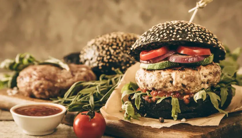 Soczysty burger z czarną bułką, kotletem, warzywami i sosem.