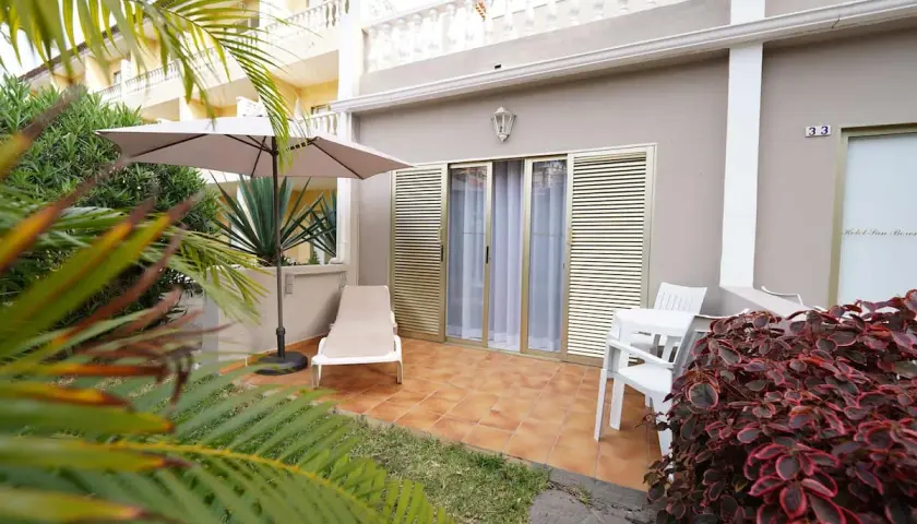 Terraza privada en el Hotel San Borondon con tumbona, sombrilla y mesa. Palmeras y vegetación exuberante rodean el espacio.