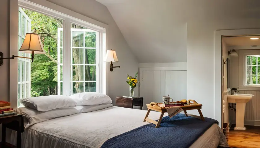 Cozy guest room decor with a bed, breakfast tray, and a window overlooking lush greenery.