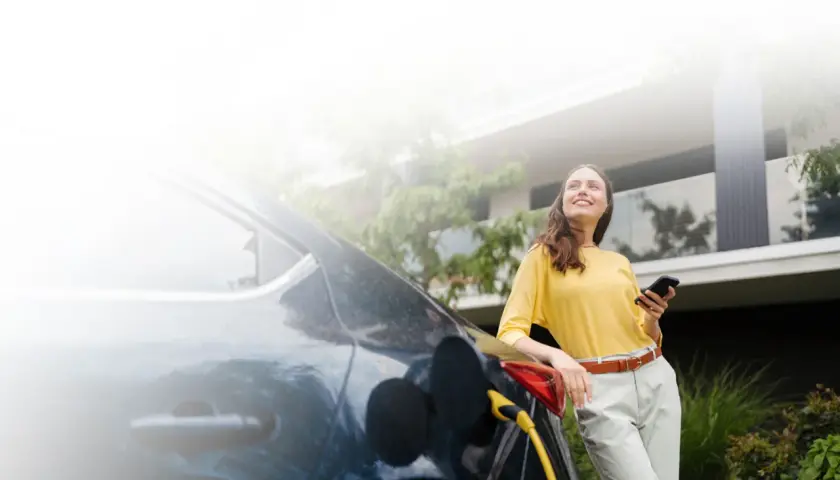 Mujer sonríe mientras carga su coche eléctrico, una elección sostenible que marca la diferencia entre híbrido y eléctrico.