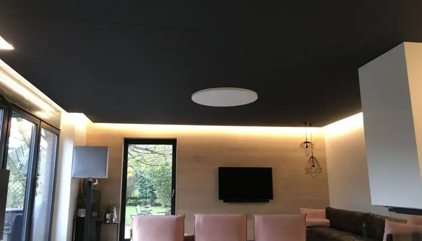 Ciemny sufit napinany z subtelnym oświetleniem LED. W salonie różowe kanapy, czarna skórzana sofa i telewizor.