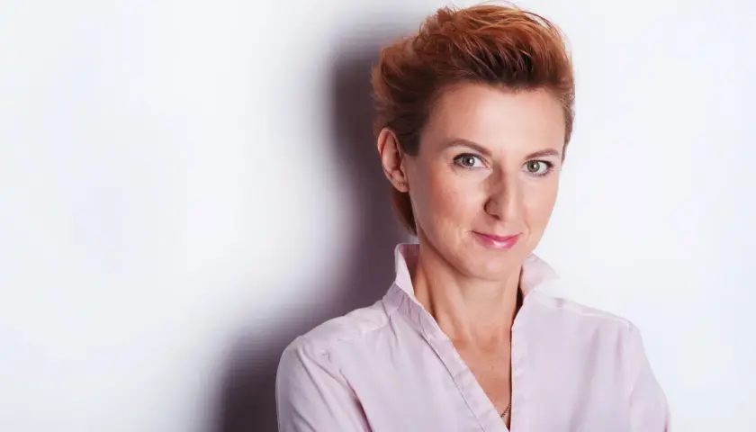 Kobieta z rudymi włosami w jasnoróżowej koszuli, uśmiecha się do obiektywu. Idealne miejsce do robienia zdjęć.