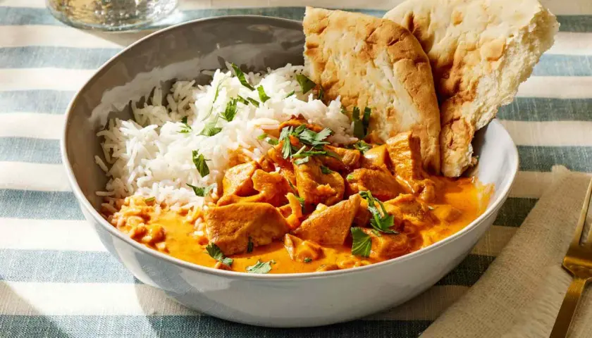 Miseczka pełna aromatycznego kurczaka butter chicken z ryżem i chlebkiem naan.