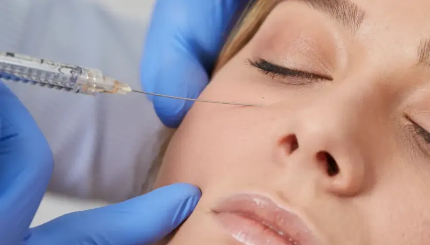 Närbild på en kvinna som får en tear trough behandling. En spruta med nål förs in under ögat för att minska mörka ringar.