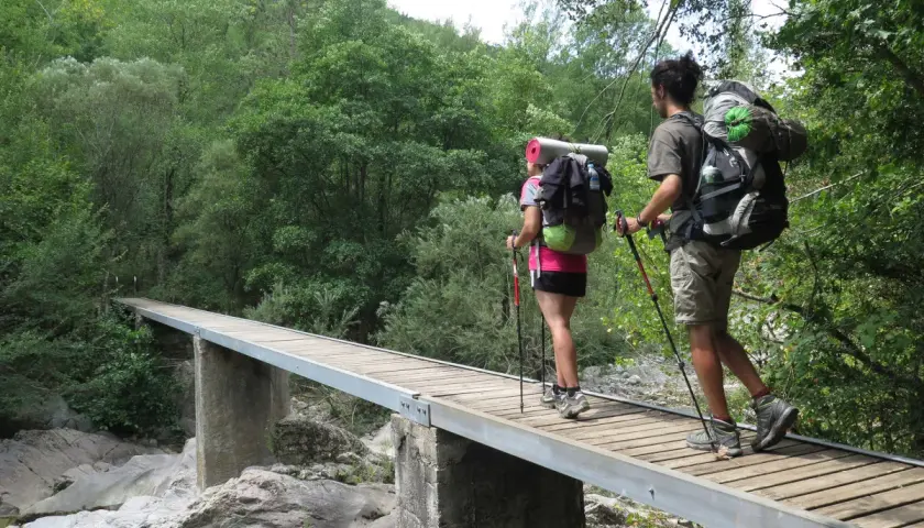 Dos excursionistas con mochilas cruzan un puente de madera en una ruta transpirenaica.