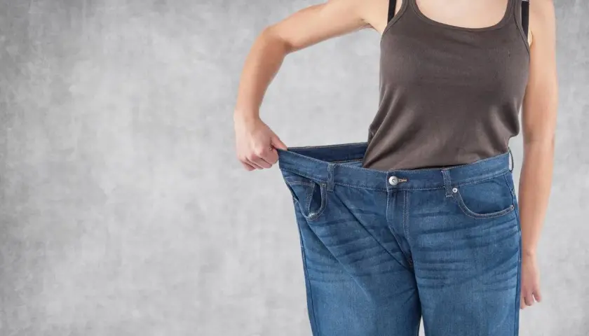 Erfolg beim Gewichtsverlust: Eine Person hält ihre viel zu große Jeans hoch, ein deutliches Zeichen für erreichten Gewichtsverlust.
