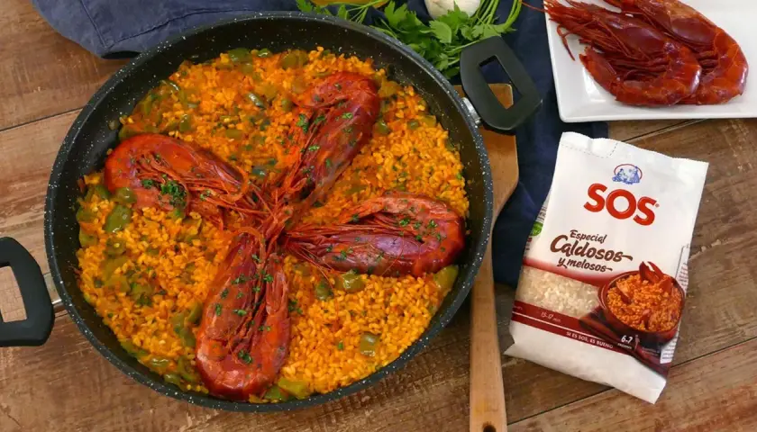 Arroz con carabineros en paellera, con pimientos verdes y perejil picado. A un lado, carabineros frescos y un paquete de arroz SOS.