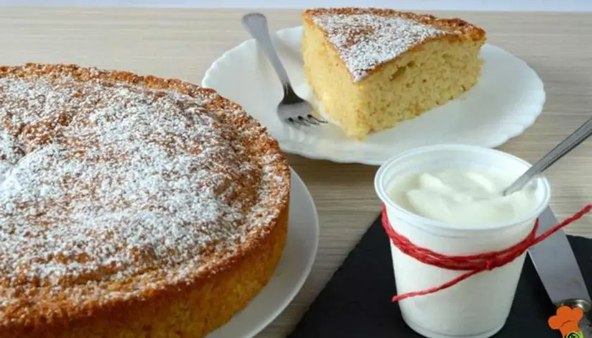 Torta 7 vasetti soffice e profumata, spolverata di zucchero a velo. Una fetta invitante e una coppetta di yogurt completano la scena.