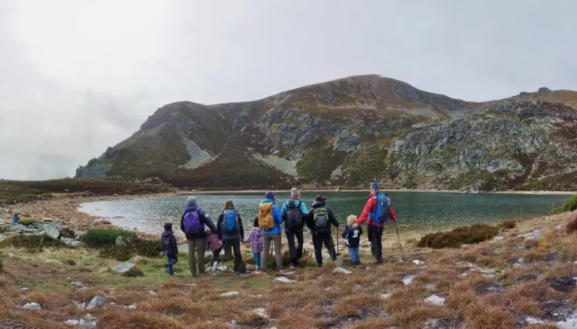 Un grupo de personas, incluyendo niños, disfruta de excursiones en familia junto a un lago rodeado de montañas.