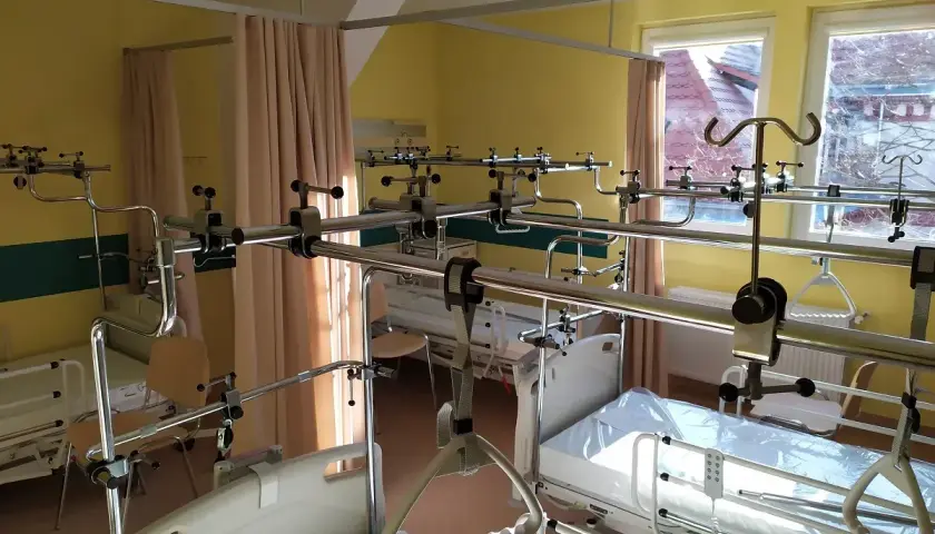 Pokój szpitalny z łóżkami i systemem poręczy nad łóżkami.