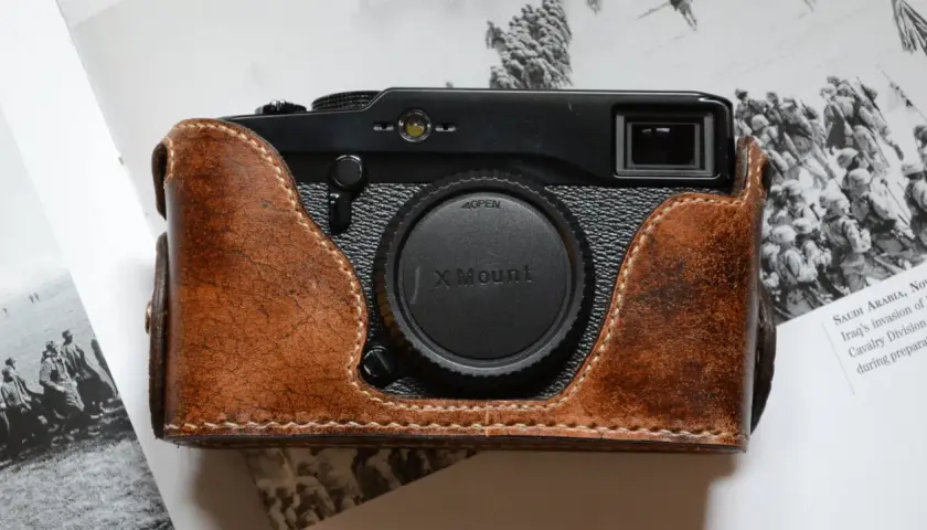 Skórzane etui na aparat Fujifilm X Pro1, z widocznym obiektywem X Mount, leży na stronach książki z historycznymi zdjęciami.